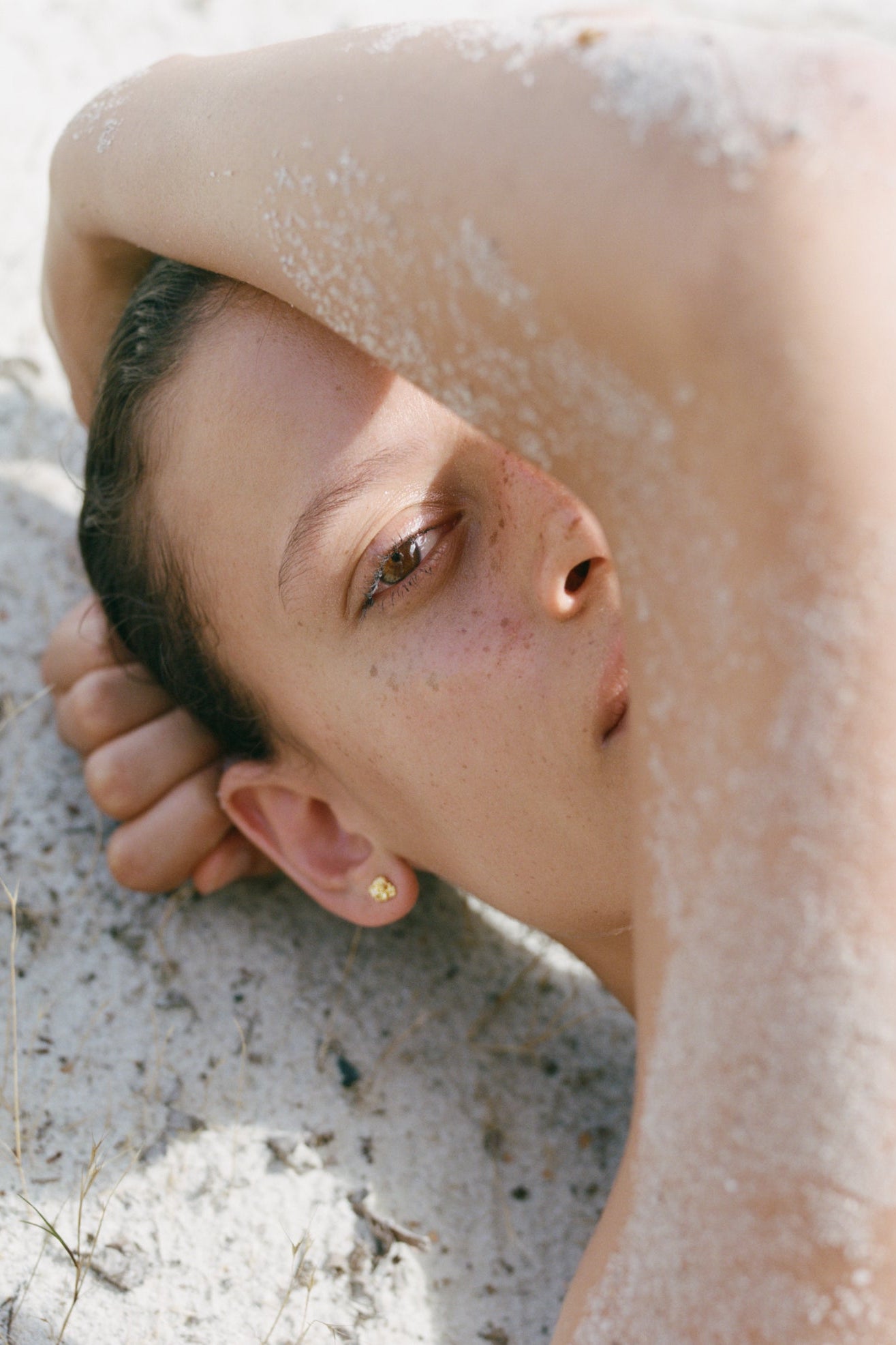 A woman lying on the sand wearing gold Honegger jewellery