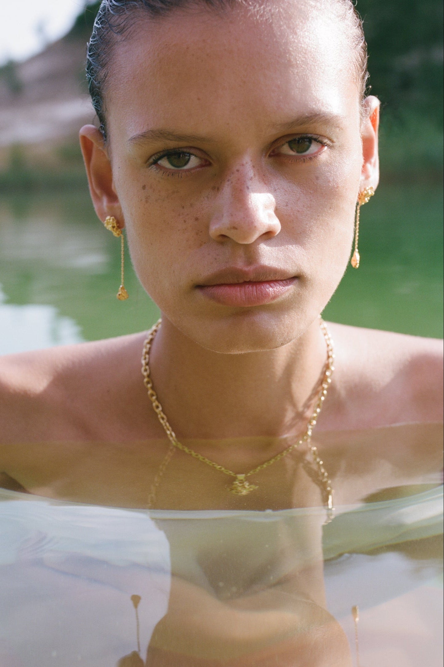 Femme portant des bijoux Honegger en or dans une rivière avec un décor naturel