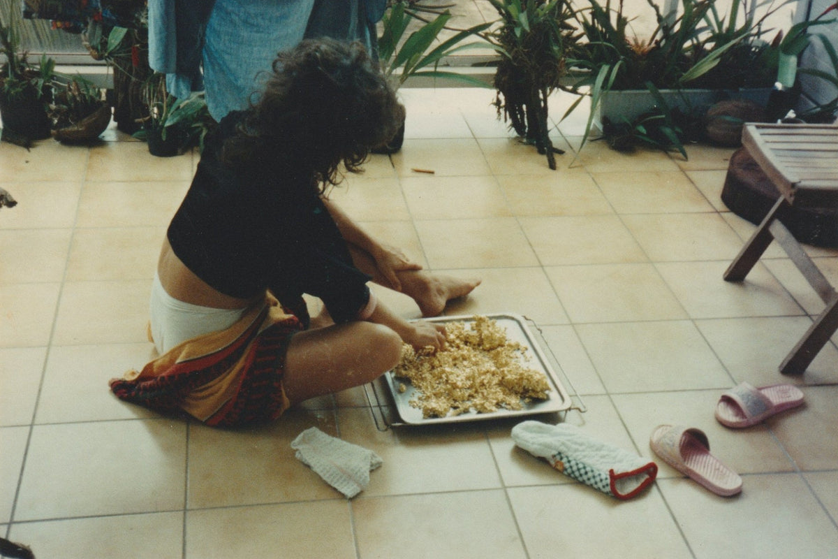 Person sitting on a tiled floor with a tray of gold, surrounded by plants.