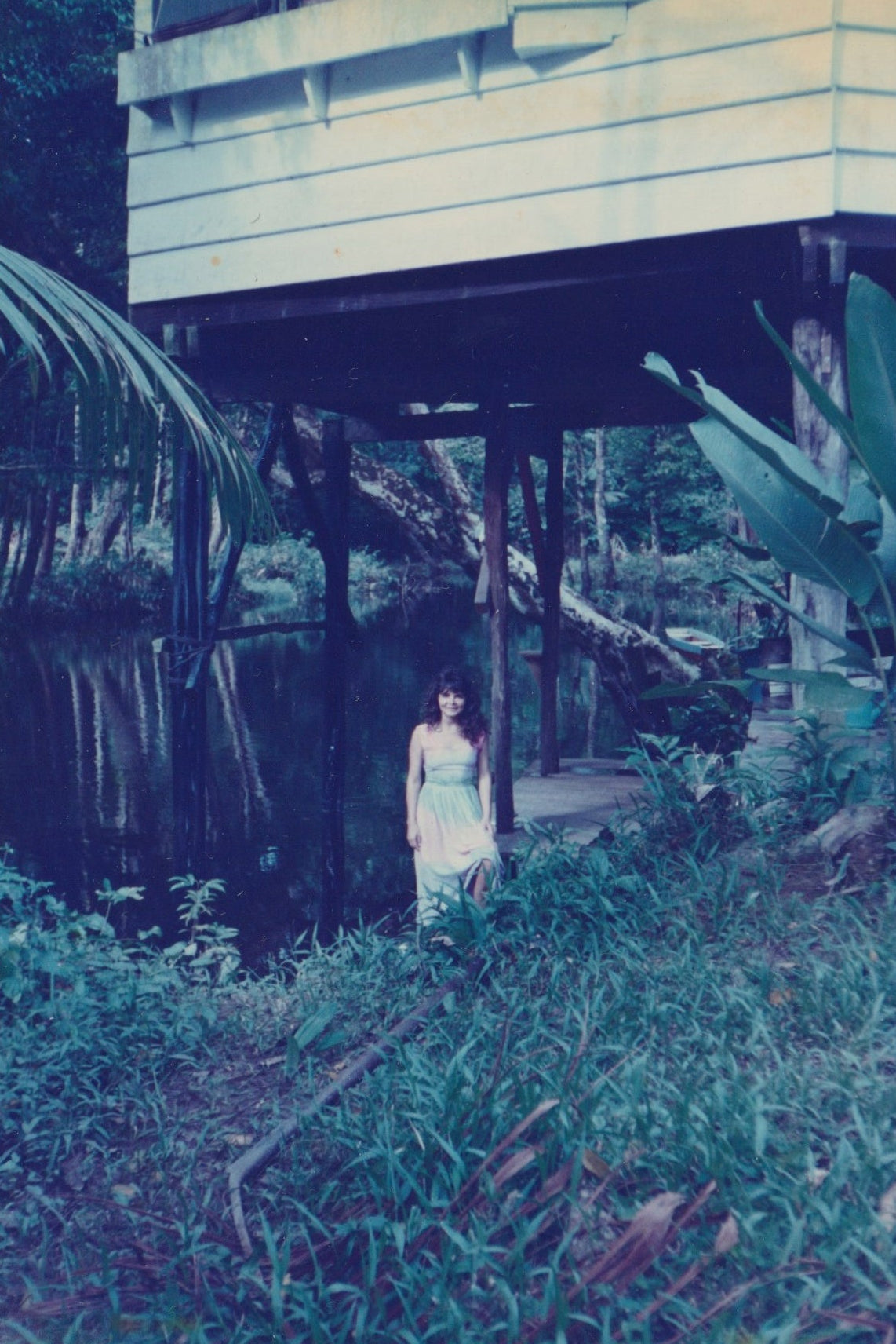 Person standing beneath a building beside a river surrounded by greenery